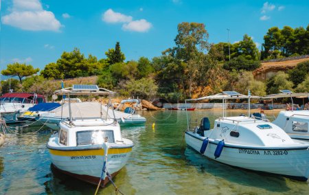 Téléchargez les photos : Vouliagmeni, Grèce - 1er septembre 2022 : Quelques bateaux amarrés dans un petit port à Vouliagmeni, Grèce, à côté d'une petite grotte où les gens profitent du beau temps d'une journée d'été - en image libre de droit