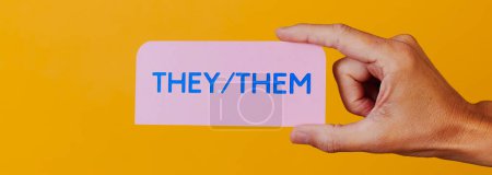 Téléchargez les photos : Personne tenant un panneau en papier rose avec le texte qu'ils, eux écrit en bleu, sur un fond orange, dans un format panoramique à utiliser comme bannière Web ou en-tête - en image libre de droit