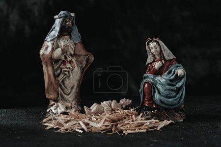 Téléchargez les photos : La sainte famille, de saint Joseph, la Vierge Marie et l'enfant Jésus sur un tas de paille, sur une surface gris foncé, sur un fond noir - en image libre de droit
