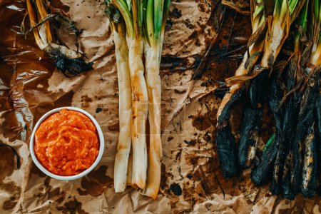 Photo for High angle view of some roasted calcots, sweet onions typical of Catalonia, Spain, some of them peeled, and a ceramic bowl with some romesco sauce to dip them in it - Royalty Free Image