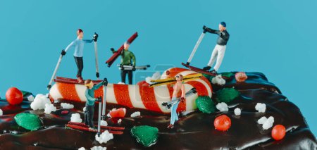 Foto de Algunas personas en miniatura esquiando o llevando sus esquís, en un pastel de tronco de yule sobre un fondo azul, en un formato panorámico para usar como banner web o cabecera - Imagen libre de derechos