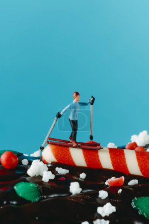 Téléchargez les photos : Gros plan d'un skieur miniature homme sur le dessus d'un gâteau de bûche de Noël, sur un fond bleu avec un peu d'espace vide sur le dessus - en image libre de droit