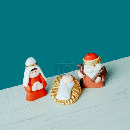 Photo for A childish depiction of the holy family, formed by the child jesus, the virgin mary and saint joseph, on a white surface, against a blue background, in a square format - Royalty Free Image