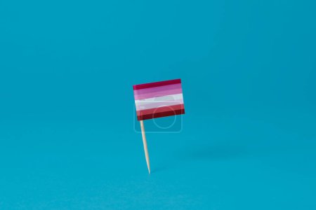 Téléchargez les photos : Gros plan d'un drapeau lesbien attaché à un poteau debout sur un fond bleu - en image libre de droit