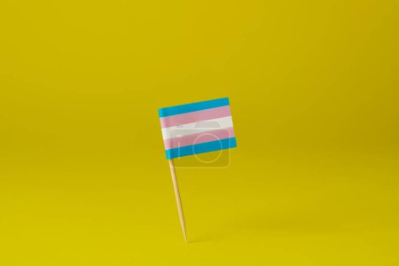 Foto de Una bandera de orgullo transgénero unida a un poste de madera colocado de pie sobre un fondo amarillo - Imagen libre de derechos