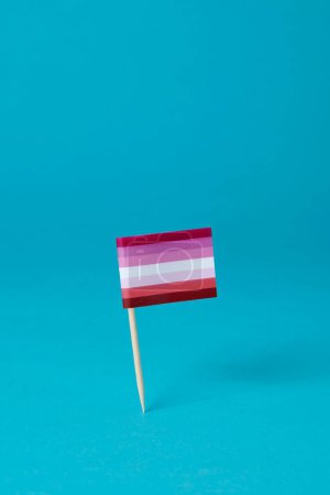 Téléchargez les photos : Un drapeau lesbien attaché à un poteau en bois se dresse sur un fond bleu, avec un peu d'espace vide sur le dessus - en image libre de droit