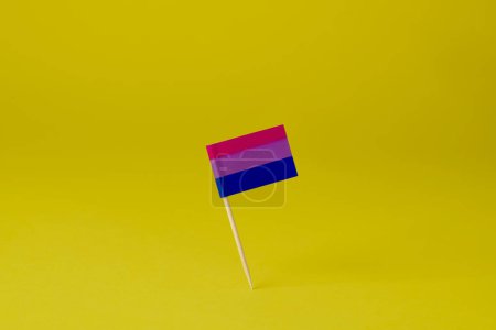Téléchargez les photos : Gros plan d'un drapeau de fierté bisexuelle attaché à un poteau debout sur un fond jaune - en image libre de droit