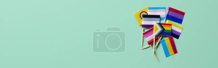 Photo for A pile of some different LGBTIQA flags attached to wooden poles on a green background in a panoramic format to use as web banner or header - Royalty Free Image