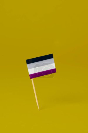 Foto de Una bandera de orgullo asexual unida a un poste de madera colocado sobre un fondo amarillo, con un poco de espacio en blanco en la parte superior - Imagen libre de derechos