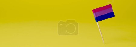Foto de Una bandera de orgullo bisexual unida a un poste de madera colocado sobre un fondo amarillo, en un formato panorámico para usar como banner web o encabezado - Imagen libre de derechos