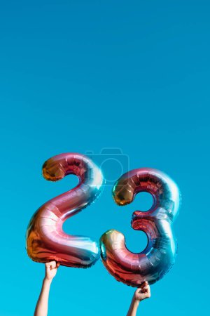 Foto de Un hombre sostiene dos globos en forma de número que forman el número 23 en el cielo azul, con un poco de espacio en blanco en la parte superior - Imagen libre de derechos