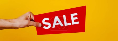 Foto de Closuep of a man holding a red sign in with the text sale, on a yellow background, in a panoramic format to use as web banner or header - Imagen libre de derechos