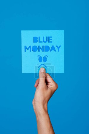Téléchargez les photos : A man holds a blue sign with the text blue monday and a sad face on a blue background - en image libre de droit