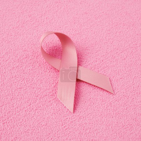 Photo for Closeup of a pink awareness ribbon, for the breast cancer awareness, on a pink textured surface - Royalty Free Image