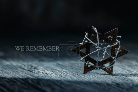 Foto de The text we remember and an old  star of david tied with some barbed wire, on a gray rustic wooden surface - Imagen libre de derechos
