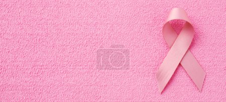 Téléchargez les photos : A pink awareness ribbon for the breast cancer awareness, on a pink textured surface, in a panoramic format to use as web banner or header - en image libre de droit