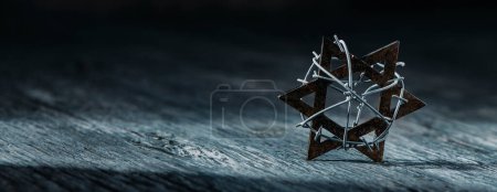 Téléchargez les photos : A star of david tied with some barbed wire placed on a gray rustic wooden surface, in a panoramic format to use as web banner or header - en image libre de droit