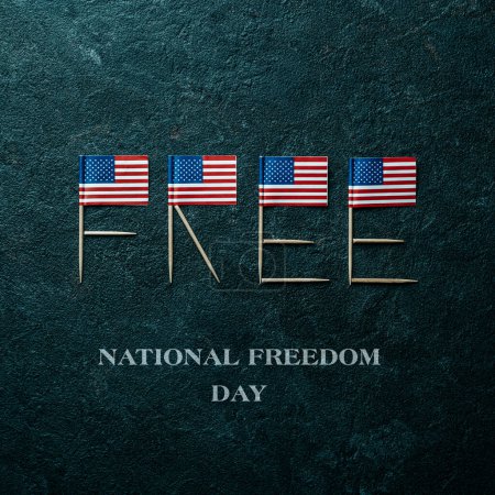 Foto de Some US flags forming the word free with their poles, and the text national freedom day on a dark gray textured background - Imagen libre de derechos