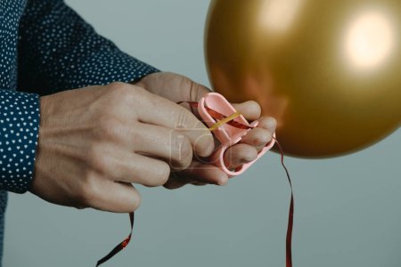 Foto de Closeup of a man using a tool to tie an inflated golden balloon to a ribbon, on a gray background - Imagen libre de derechos