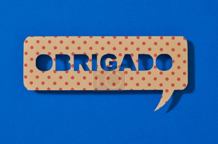 Photo for A paper sign in the shape of a speech bubble with the text thank you written in portuguese, on a blue background - Royalty Free Image
