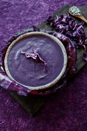 Téléchargez les photos : Vue en angle élevé d'une soupe au chou rouge dans un bol rustique en céramique, placé sur une surface texturée violette - en image libre de droit