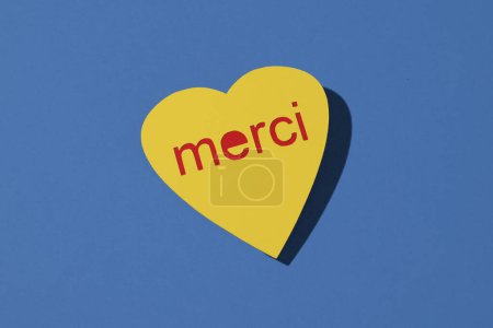 Téléchargez les photos : Gros plan d'un signe jaune en forme de coeur qui dit merci en français, sur un fond bleu - en image libre de droit