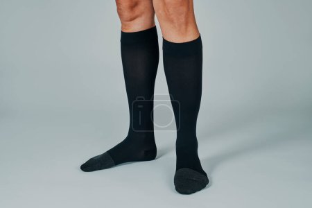 Téléchargez les photos : Closeup of a man wearing a pair of black compression socks standing on an off-white background - en image libre de droit