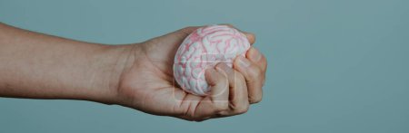 Photo for Closeup of a man is squeezing a fake brain in his hand, on a gray background with some blank space on the right, in a panoramic format to use as web banner - Royalty Free Image