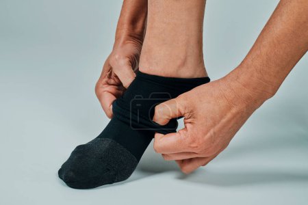 Foto de Closeup of a man putting on a compression sock, on an off-white background - Imagen libre de derechos