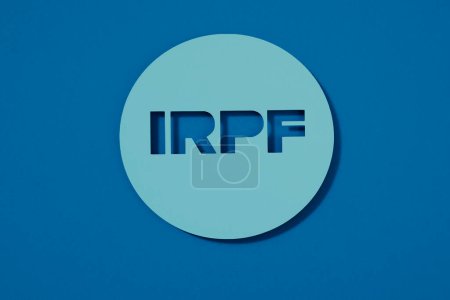 Photo for A round blue paper sign with the spanish acronym text for Impuesto sobre la Renta de las Personas Fisicas, Personal Income Tax, on a blue background - Royalty Free Image