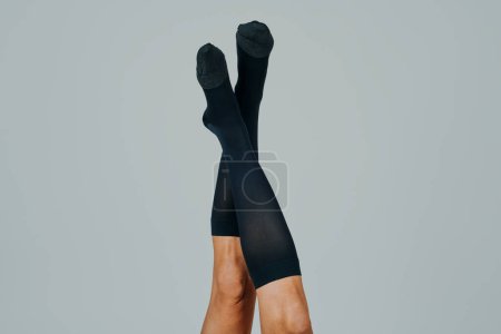 Téléchargez les photos : Les jambes d'un homme, à l'envers, portant des chaussettes de compression, devant un fond blanc cassé avec un espace vide autour de lui - en image libre de droit
