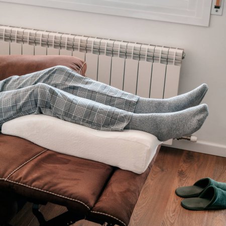 Foto de Primer plano de un hombre apoyando sus piernas en una almohada de elevación de las piernas, hecha de espuma de memoria, descansando en el sofá - Imagen libre de derechos
