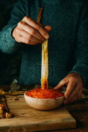 Photo for Closeup of a man dipping a roasted calcot, a sweet onion typical of Catalonia, Spain, in romesco sauce, as it is customary - Royalty Free Image