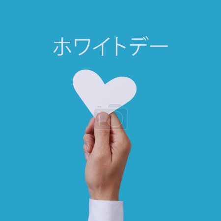 Foto de Primer plano de un hombre con un corazón blanco en la mano y el texto blanco día escrito en japonés sobre un fondo azul - Imagen libre de derechos