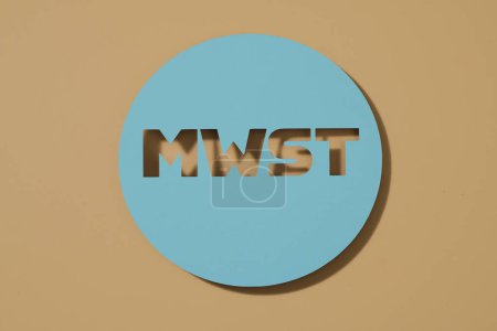 Foto de Un cartel de papel azul con el acrónimo alemán MWST, para MehrwertSteuer, impuesto sobre el valor añadido, sobre un fondo marrón - Imagen libre de derechos