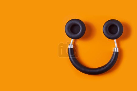 Téléchargez les photos : A pair of black wireless full size headphones upside down on an orange background, resembling a smiley face - en image libre de droit