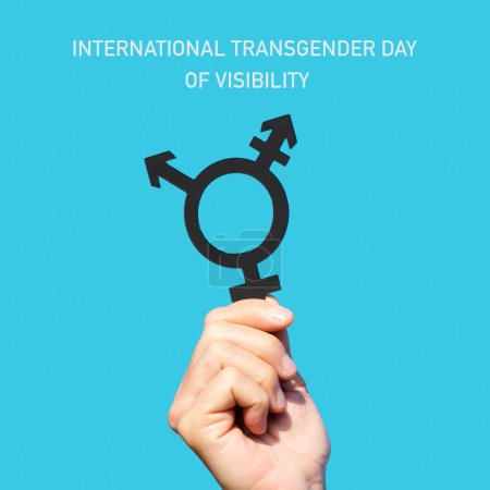 Téléchargez les photos : Le texte Journée internationale de la visibilité transgenre et la main d'un jeune caucasien tenant un symbole transgenre contre le ciel bleu - en image libre de droit