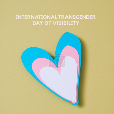 Foto de El texto internacional transgénero día de la visibilidad y un corazón con los colores de la bandera transgénero sobre un fondo amarillo pálido - Imagen libre de derechos