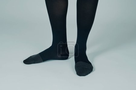 Téléchargez les photos : Gros plan des jambes d'un homme debout sur un fond blanc cassé portant une paire de chaussettes de compression noires - en image libre de droit