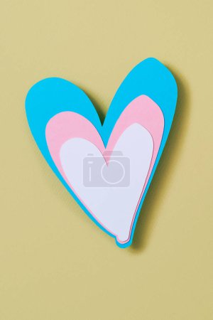 Foto de Primer plano de un corazón con los colores de la bandera transgénero, azul, rosa y blanco, sobre un fondo amarillo pálido - Imagen libre de derechos