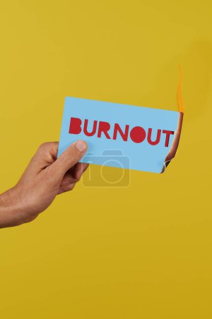 un hombre sostiene un letrero azul en llamas con el texto burnout delante de un fondo amarillo con somne espacio en blanco en la parte superior y en la parte inferior