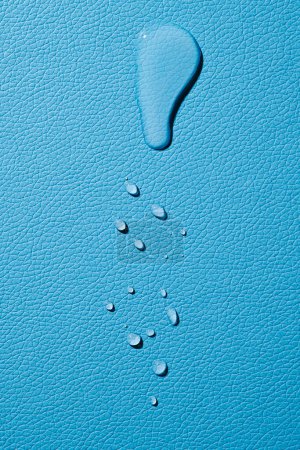 Foto de Vista de ángulo alto de una gran gota de agua y algunas otras gotas más pequeñas sobre una superficie de cuero azul - Imagen libre de derechos