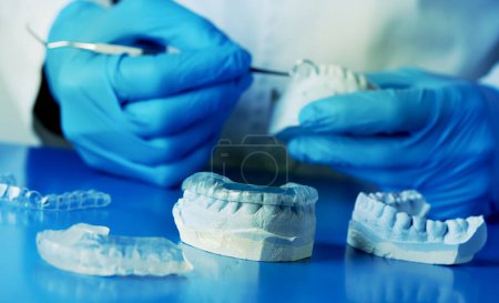 closeup of a dentist, wearing blue latex gloves, adjusting an occlusal splint, using a mouth cast