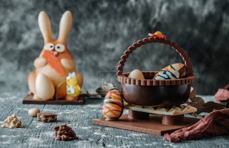 a chocolate easter bunny and a chocolate basket with eggs as a spanish mona de pascua, a traditional confection given by godparents to godchild on easter, on a gray rustic table