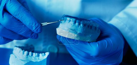 Photo for A technician, wearing blue latex gloves, adjusting an occlusal splint, in a panoramic format to use as web banner or header - Royalty Free Image