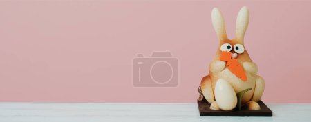 Téléchargez les photos : Un lapin en chocolat comme moine de pascua espagnol, une confiserie traditionnelle donnée par les parrains au filleul à Pâques, sur une table sur fond rose, dans un format de bannière panoramique - en image libre de droit