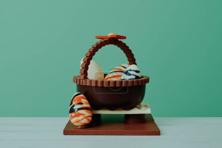 Photo for A chocolate basket with eggs as a spanish mona de pascua, a traditional confection given by godparents to godchild on easter, on a wooden table against a green background - Royalty Free Image