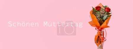Téléchargez les photos : Un homme tient à la main un bouquet de roses rouges et le texte joyeuse fête des mères écrit en allemand sur fond rose, dans un format panoramique à utiliser comme bannière web - en image libre de droit