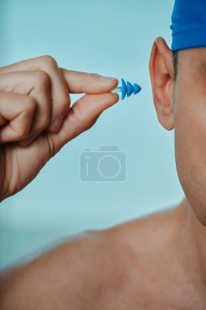 Photo for A swimmer man, wearing a blue swimming cap, puts an earplug in his ear, in a swimming pool - Royalty Free Image