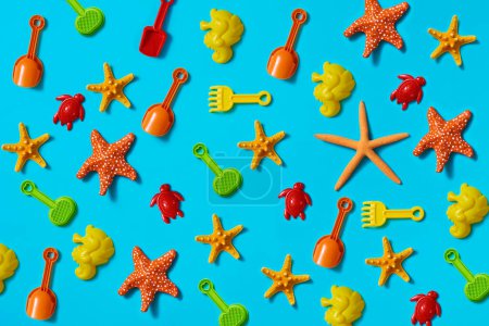Téléchargez les photos : Quelques pelles et raquettes de plage, quelques moules de sable en forme d'hippocampes et de tortues, et quelques étoiles de mer naturelles et fausses sur fond bleu - en image libre de droit